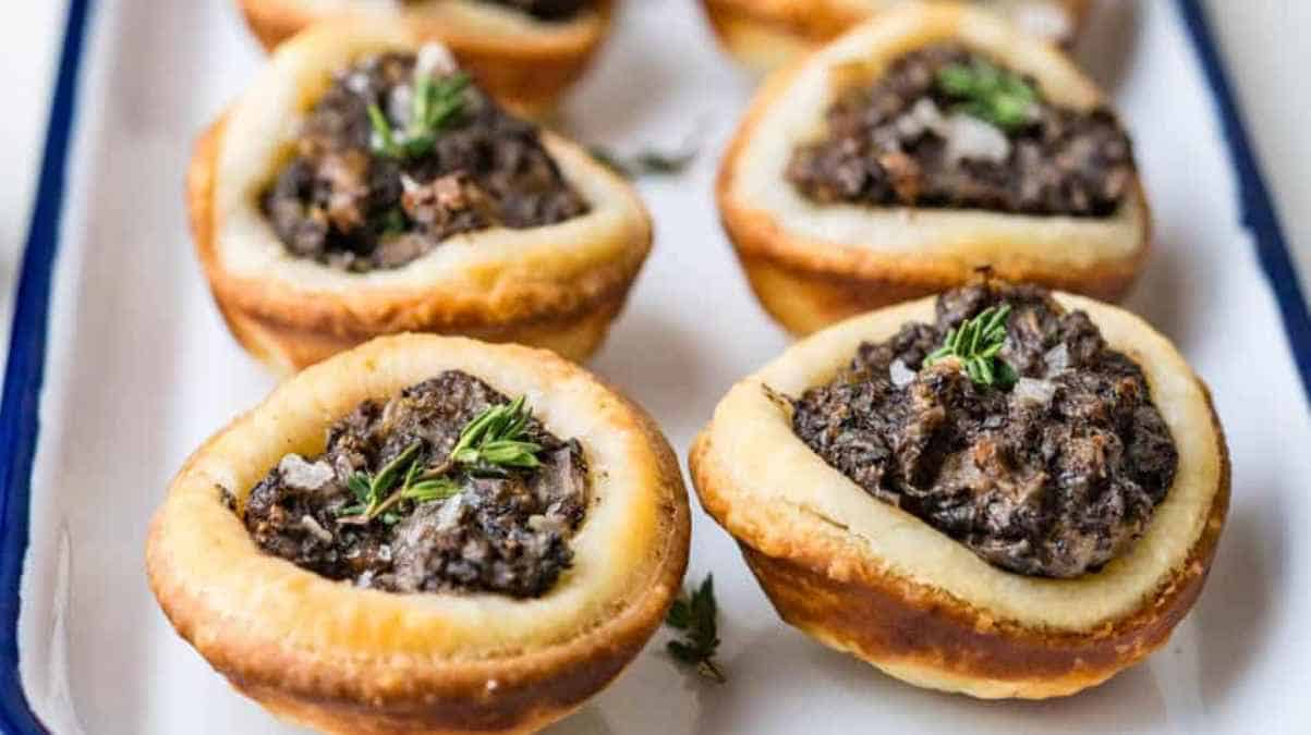A tray of savory mushroom tartlets garnished with fresh herbs.