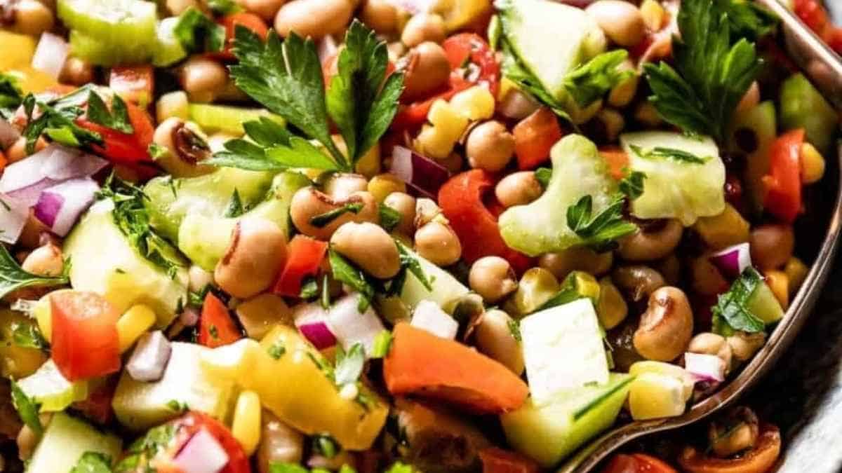A colorful mixed bean salad with cucumbers, tomatoes, corn, and parsley, topped with a light dressing.