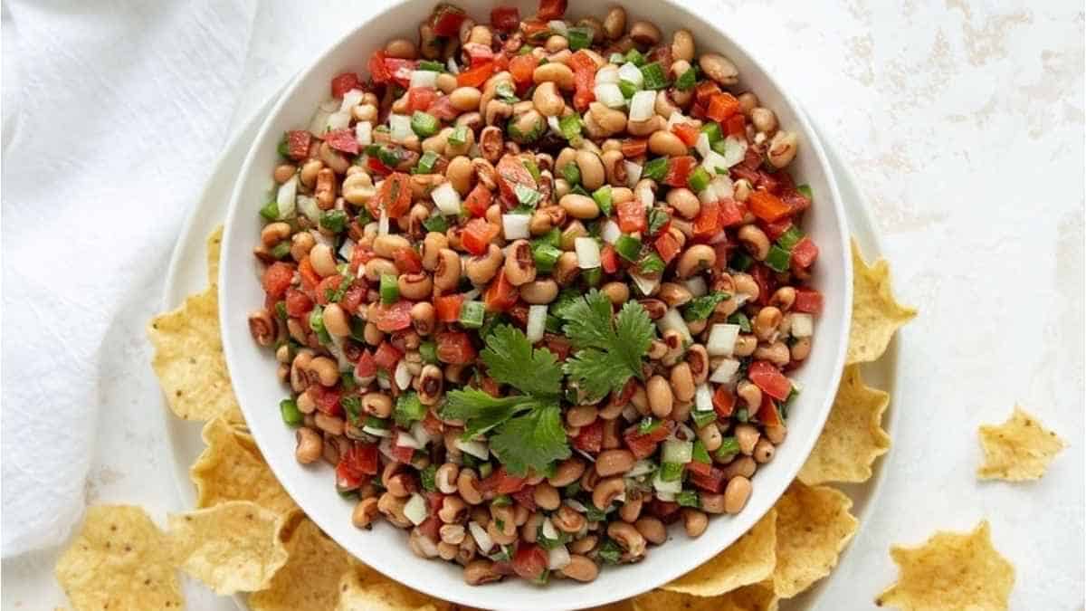 A bowl of black-eyed pea salad garnished with fresh herbs, surrounded by tortilla chips.