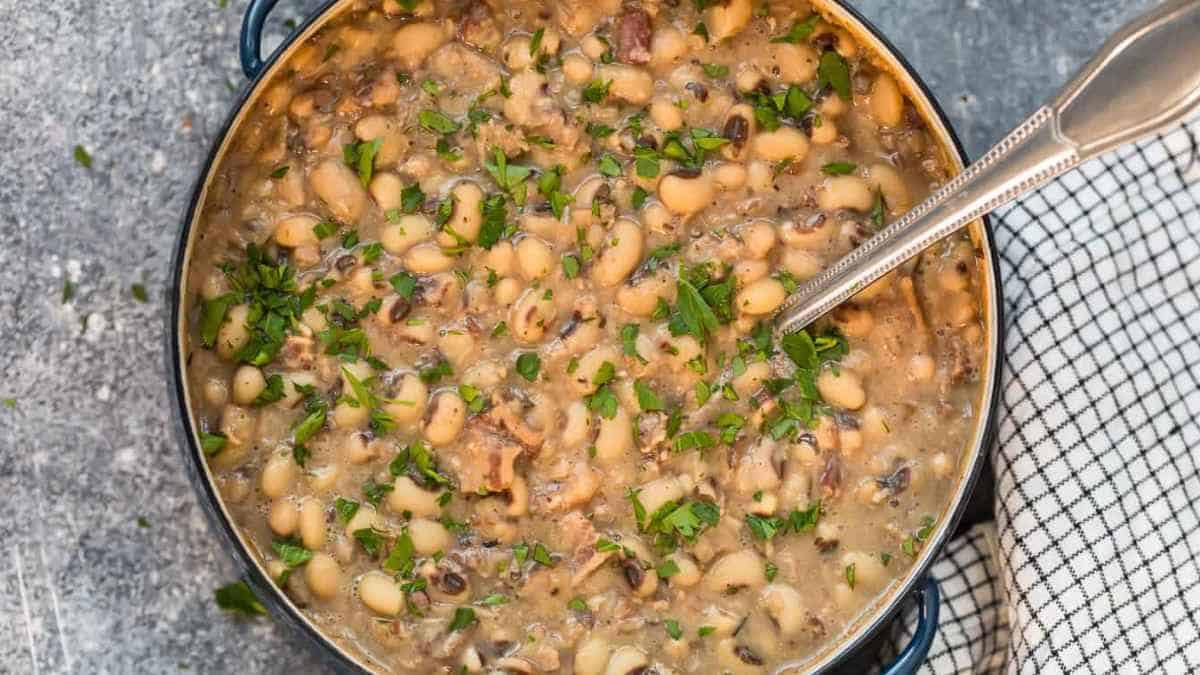 Pot of white bean soup garnished with fresh herbs next to a patterned napkin.