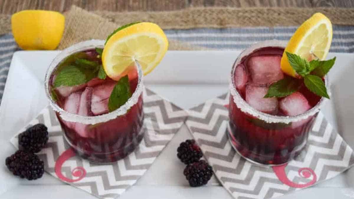 Two blackberry margaritas with lemon and mint garnishes.