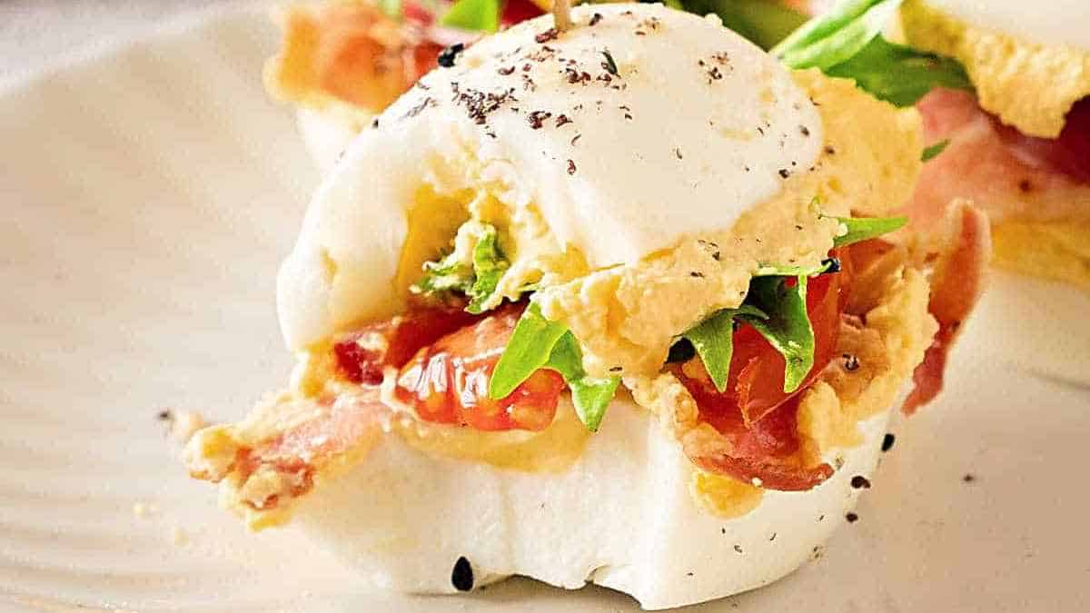 A poached egg atop a bed of arugula and bacon, seasoned with black pepper, on an open-faced sandwich.