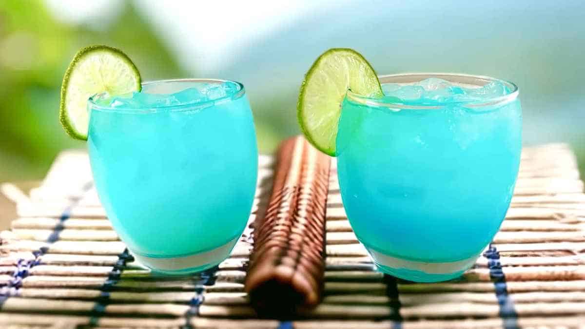 Two glasses of blue drink with lime wedges.