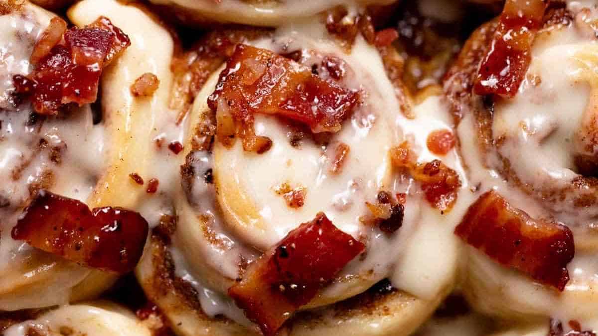 Close-up of cinnamon rolls topped with cream cheese frosting and bacon bits.