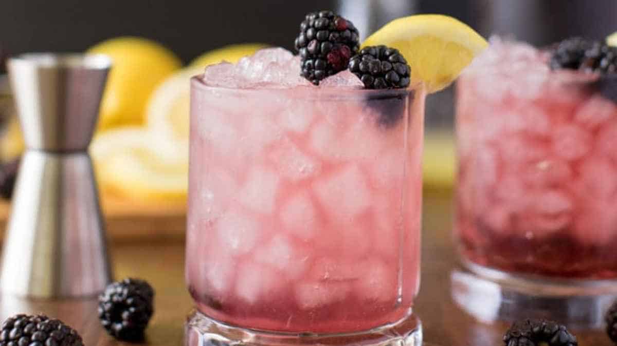 Two glasses of blackberry lemonade with lemon slices and blackberries.