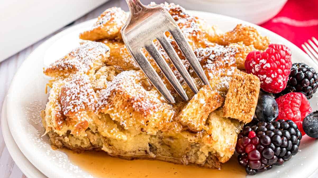 French toast casserole with fresh berries and a dusting of powdered sugar, served on a white plate with a fork.