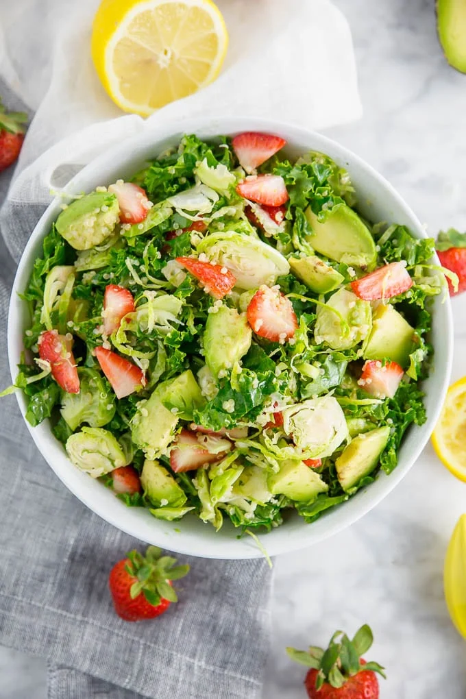 A bowl of brussels sprout kale salad with avocado, quinoa and strawberries. 
