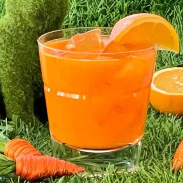 A glass of orange juice and carrots on the grass.