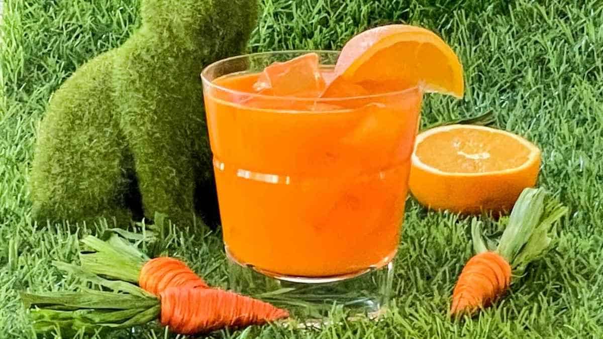 A glass of orange juice and carrots on the grass.