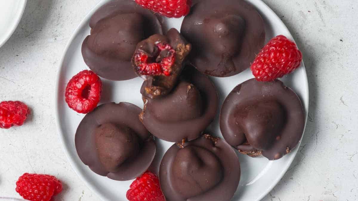 Chocolate-covered treats with raspberries on a white plate.