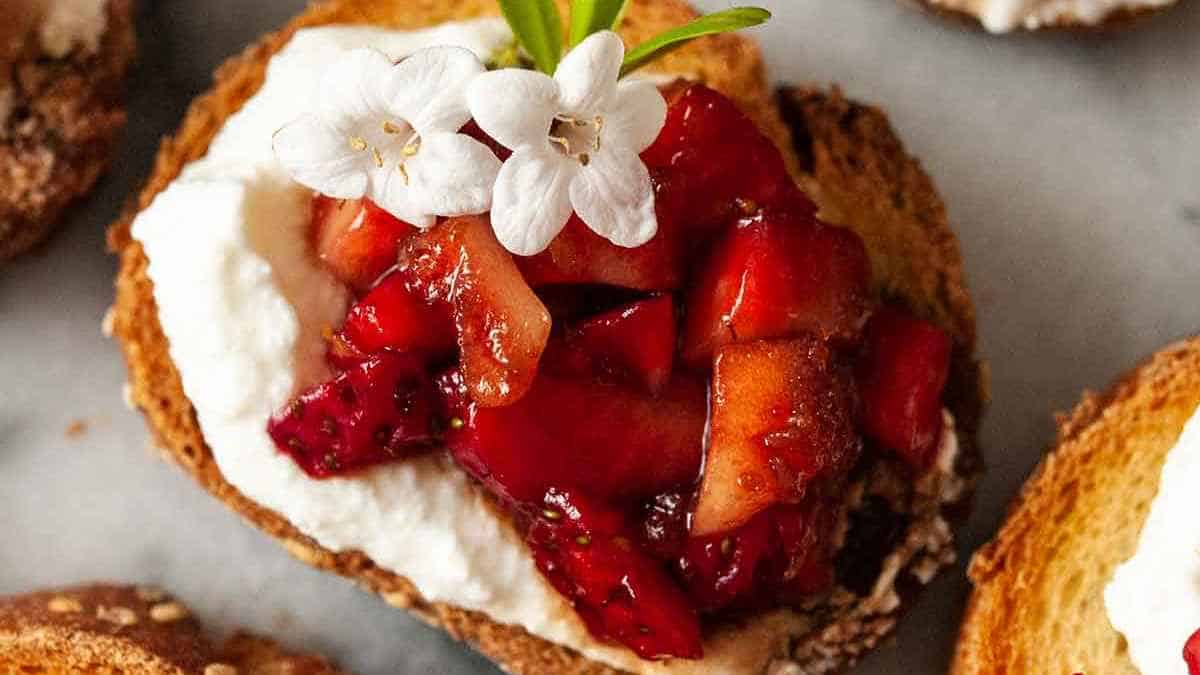 Toasted bread topped with creamy spread and glazed strawberries, garnished with a white flower.