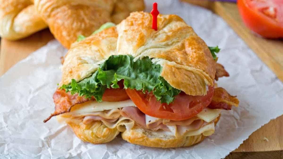 A turkey and bacon sandwich with lettuce and tomato served on a croissant.