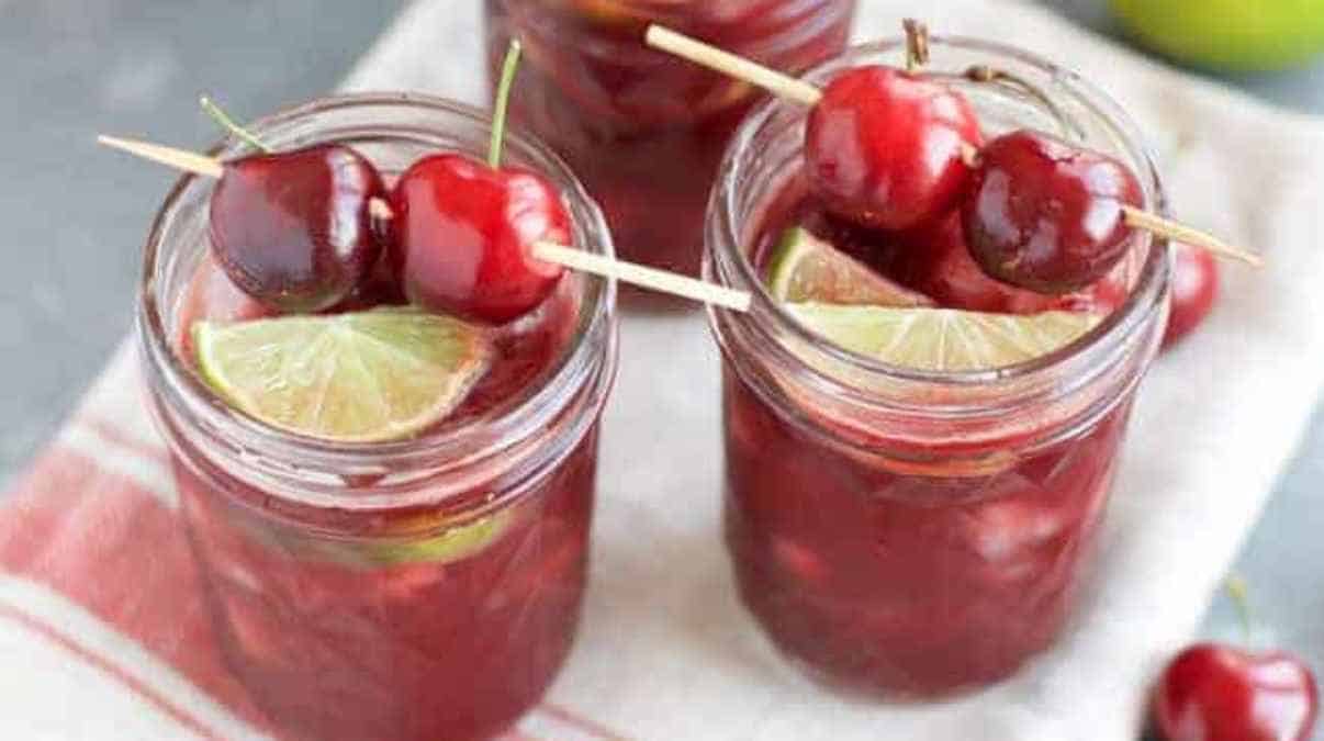 Three jars of cherry sangria with limes and cherries.