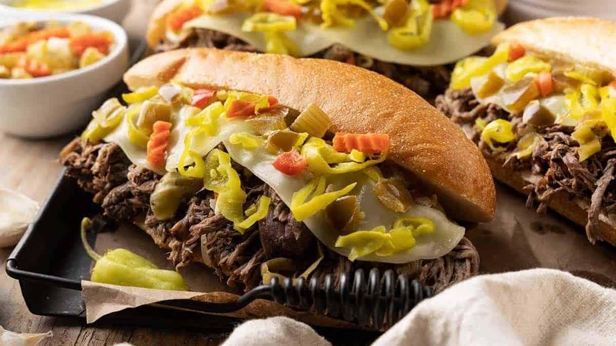 Italian beef sandwiches topped with melted cheese and giardiniera on a tray.