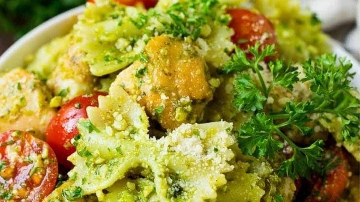 A bowl of pesto pasta with chicken and tomatoes.
