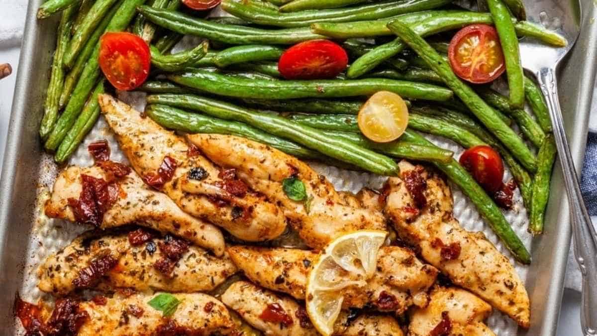 Grilled chicken with green beans and tomatoes on a baking sheet.