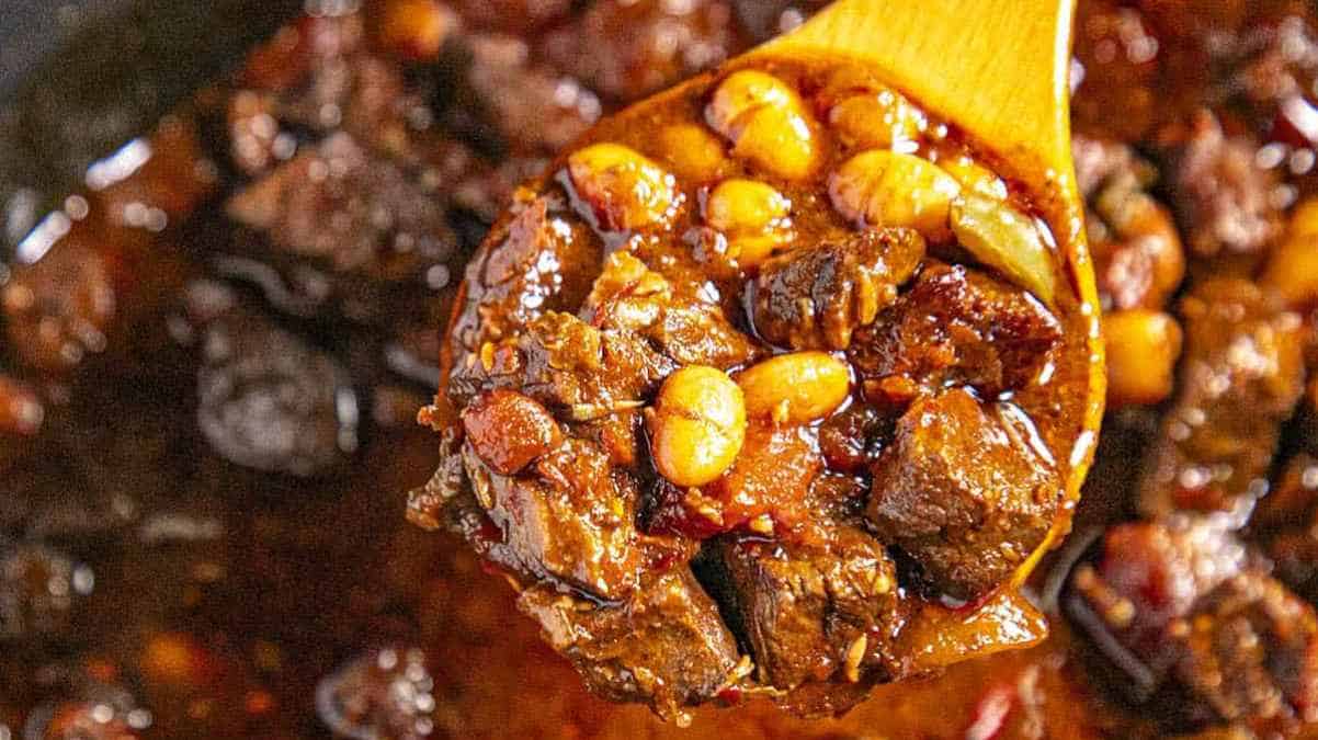 Beef chili with beans being scooped up by a wooden spoon.