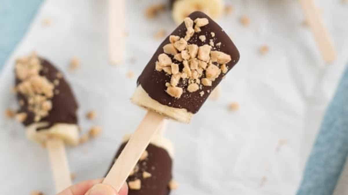 Chocolate-covered ice cream bars sprinkled with crushed nuts on a light blue background.