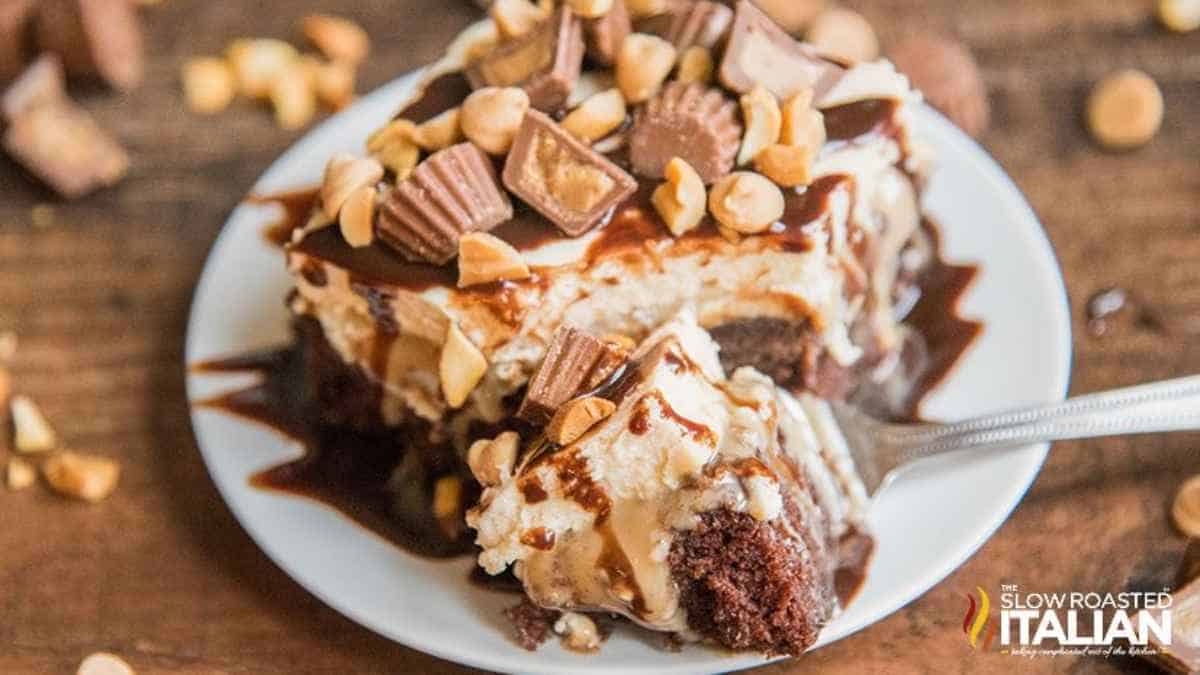 A plate of decadent layered dessert with chocolate cake, ice cream, chopped nuts, chocolate pieces, and drizzled with caramel sauce.