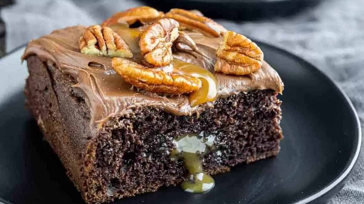 A slice of chocolate cake with caramel topping and pecans on a plate.