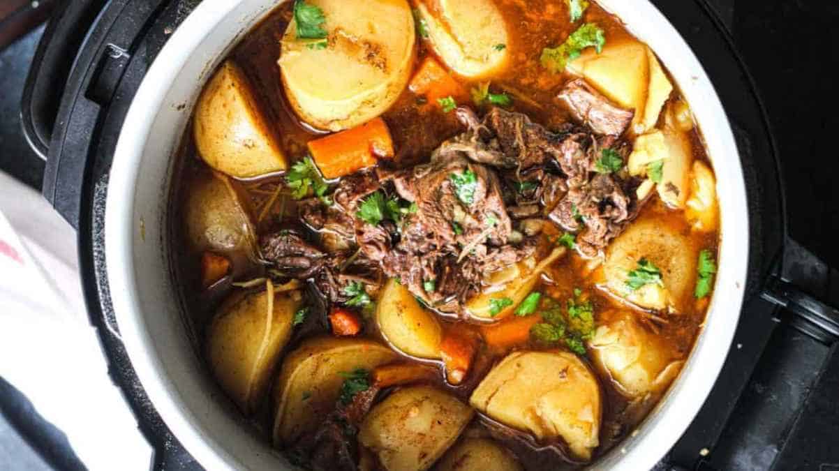 Beef stew with potatoes and carrots in a white pot.