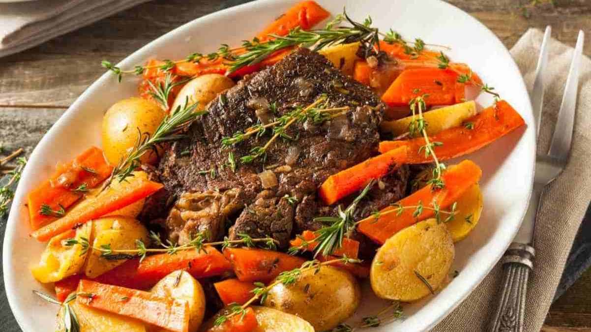 Hearty pot roast with carrots, potatoes, and fresh herbs served on a white plate.