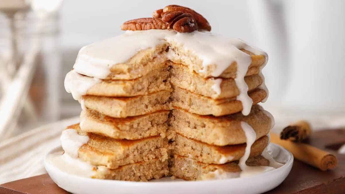 A stack of cinnamon pancakes topped with white icing and pecans on a white plate.