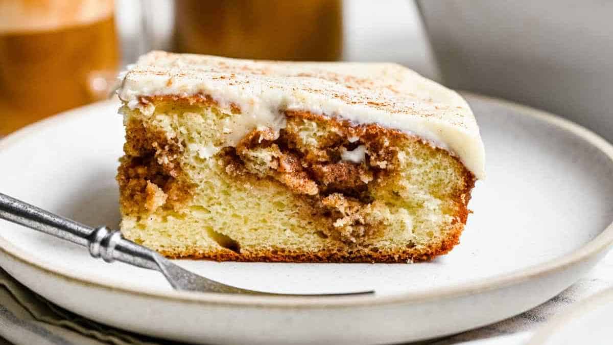 A slice of frosted cinnamon coffee cake on a white plate with a fork.