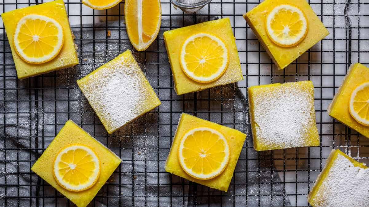 Lemon bars dusted with powdered sugar on a cooling rack with lemon slices as garnish.