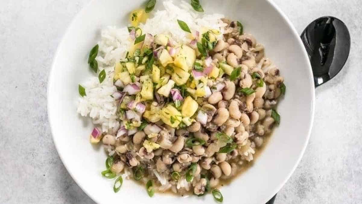 A plate of rice topped with black-eyed peas and garnished with herbs and diced vegetables.