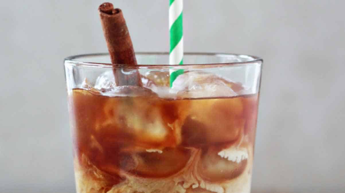 A glass of iced coffee with a cinnamon stick and a striped straw.