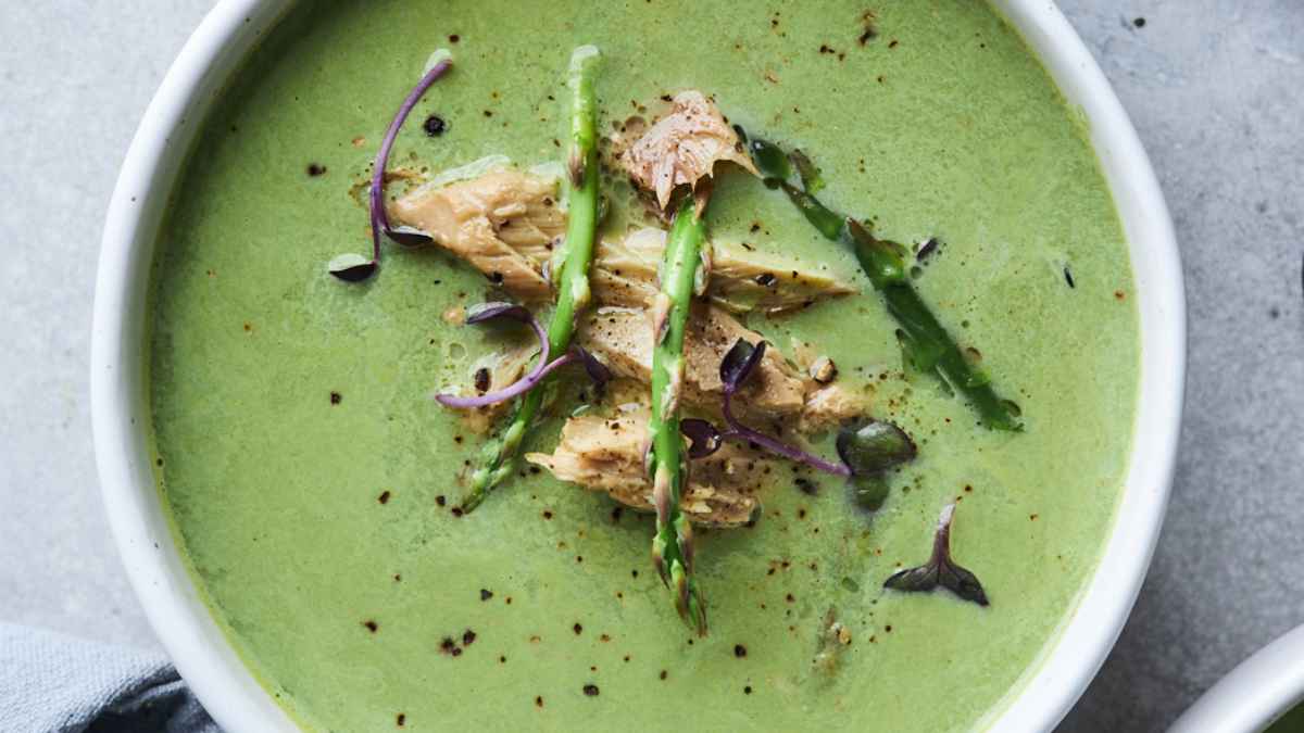 یک کاسه سوپ سبز خامه ای که با مارچوبه، گیاهان و ادویه جات تزیین شده است.