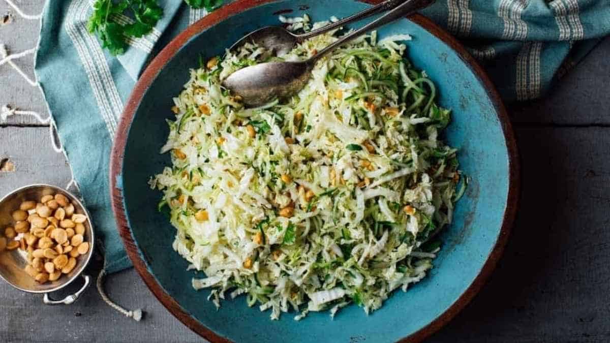 A bowl of cabbage slaw with peanuts and a spoon.