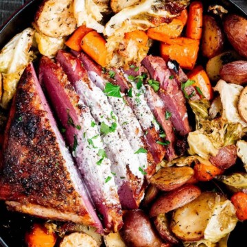 Roasted vegetables and meat in a skillet garnished with fresh herbs.