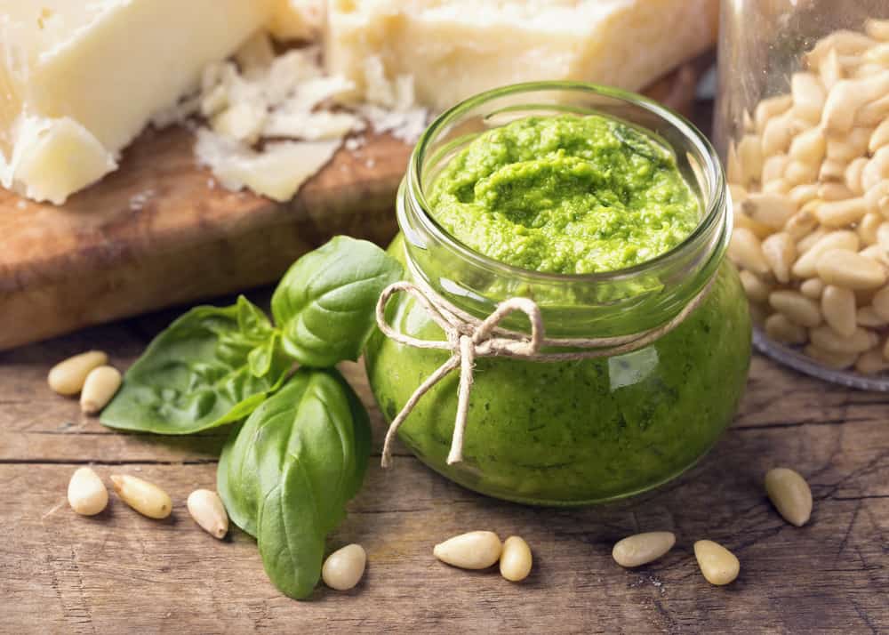 A jar of pesto with basil and cheese on a wooden table.
