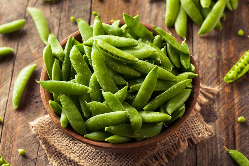 A bowl of peas on a wood surface.