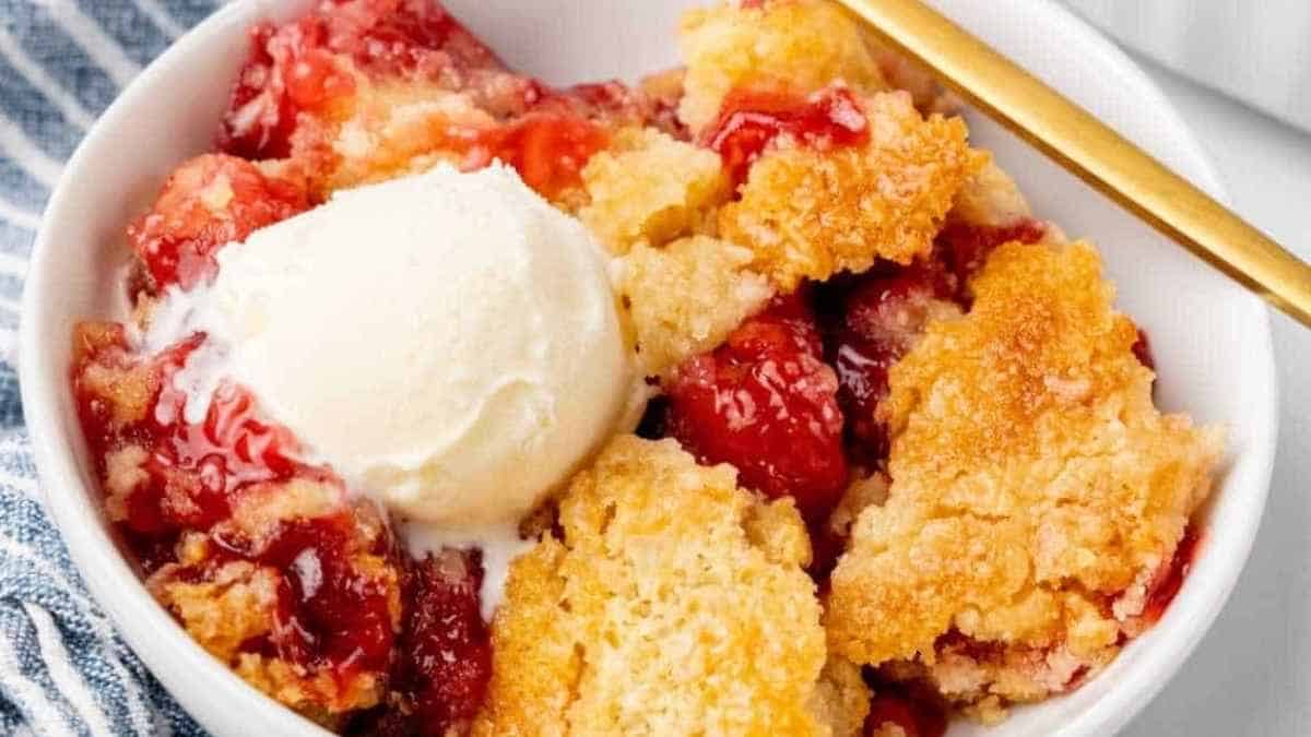 Strawberry cobbler in a white bowl with a scoop of ice cream.