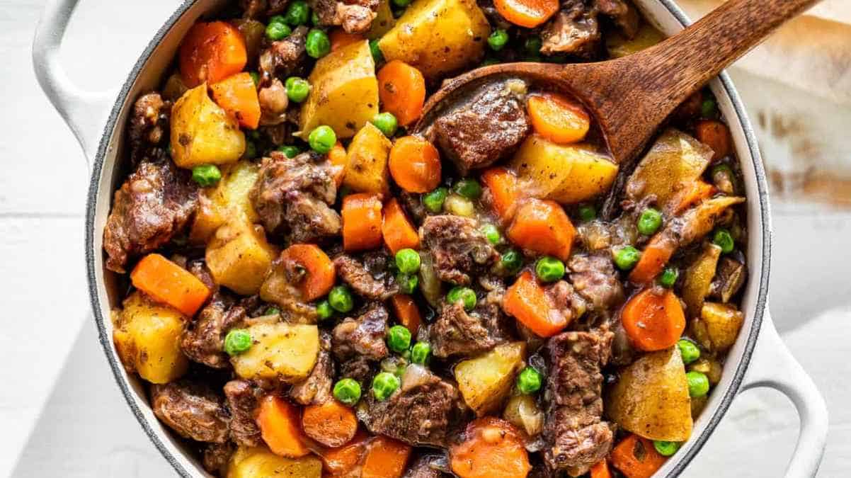 A skillet containing a hearty beef stew with potatoes, carrots, and peas.