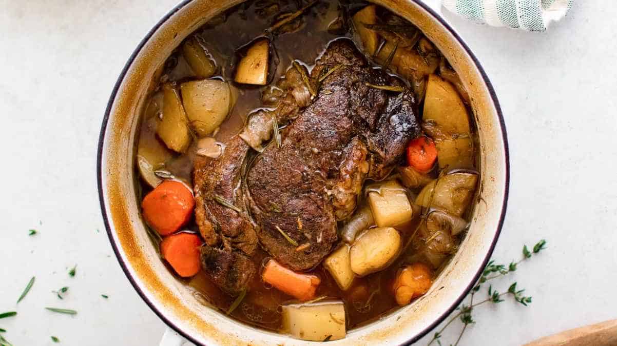 A bowl of beef stew with carrots, potatoes, and herbs.