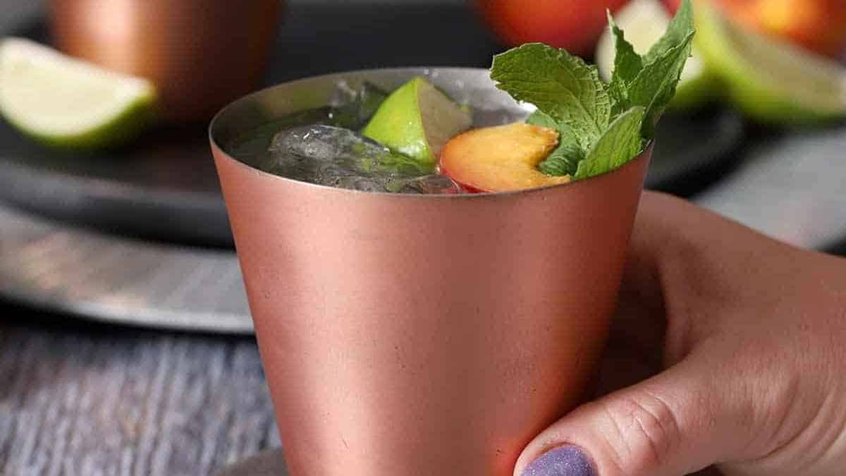 A person holding a copper cup with a lime and peach garnish.