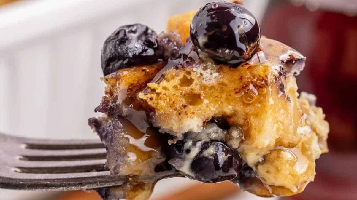 A fork lifting a bite of blueberry pancake dripping with syrup.