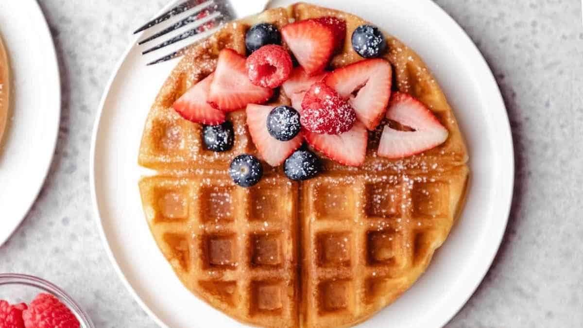 A freshly made waffle topped with strawberries and blueberries on a white plate.