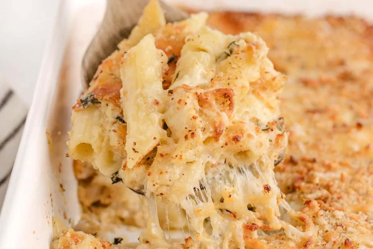 A serving of creamy baked macaroni and cheese with a crispy topping being lifted from a casserole dish, revealing melted cheese strands.