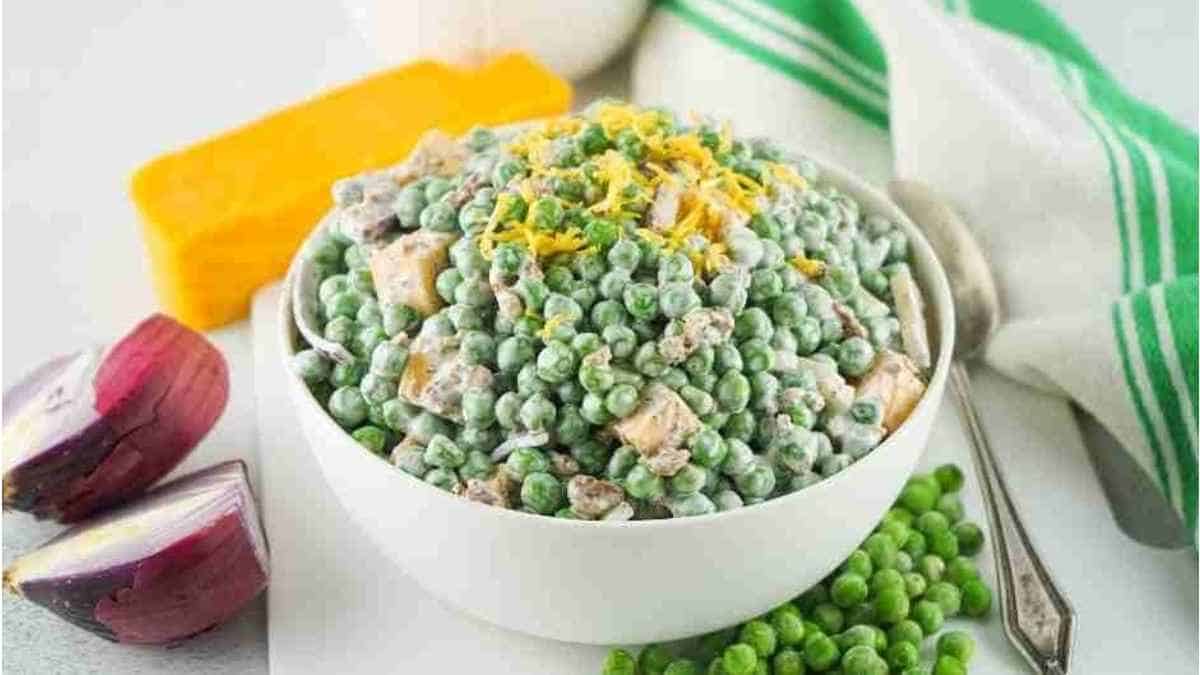 Pea salad in a white bowl with onions and cheese.
