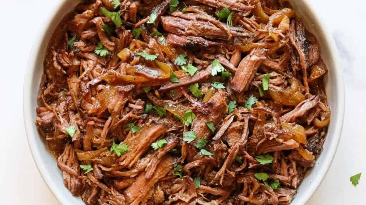 A bowl of pulled meat garnished with herbs.