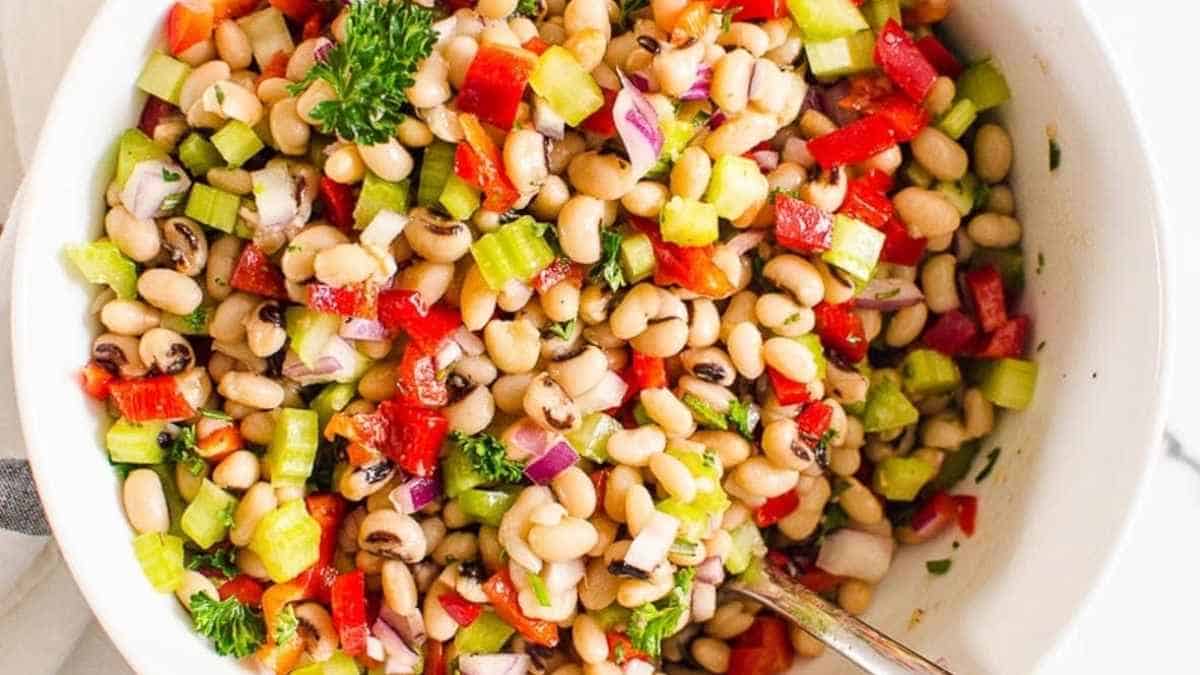A colorful mixed bean salad with chopped vegetables in a white bowl.
