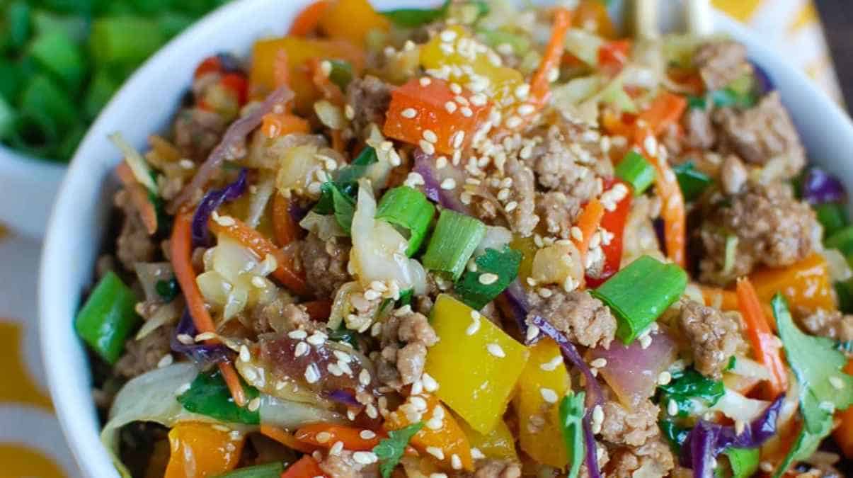 A bowl of stir-fried vegetables and ground meat garnished with sesame seeds and green onions.