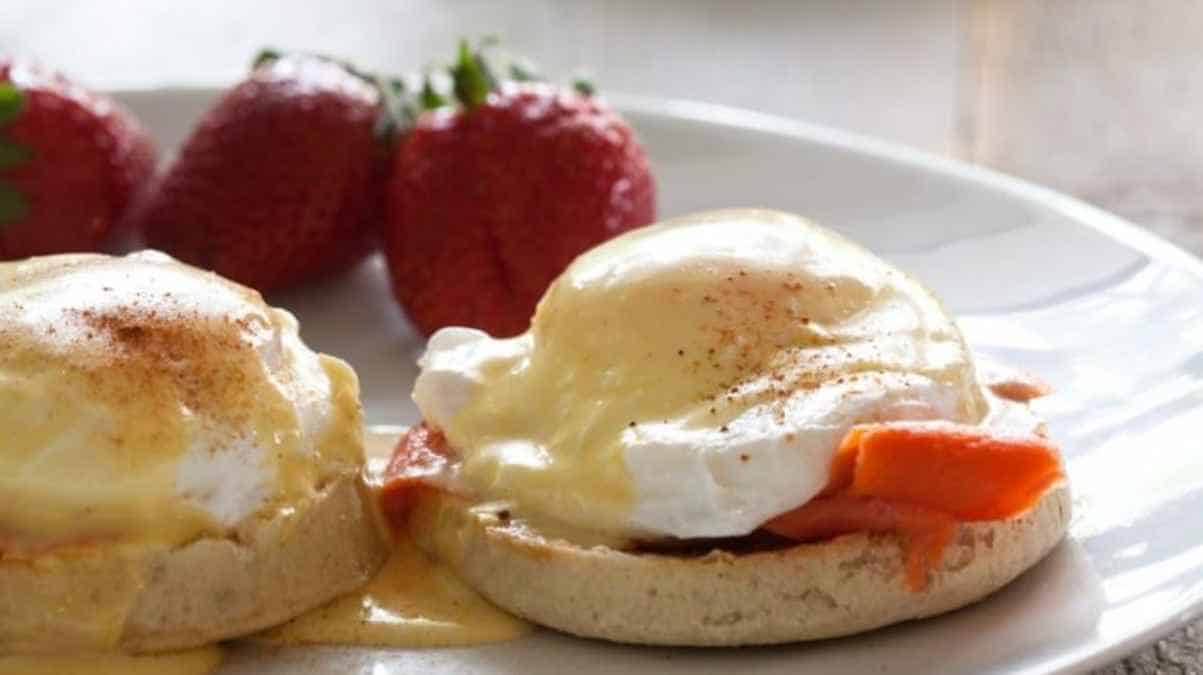 Plate of eggs benedict with smoked salmon and a side of strawberries.