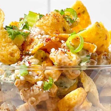 A bowl of creamy pasta salad garnished with herbs and topped with crunchy corn chips.