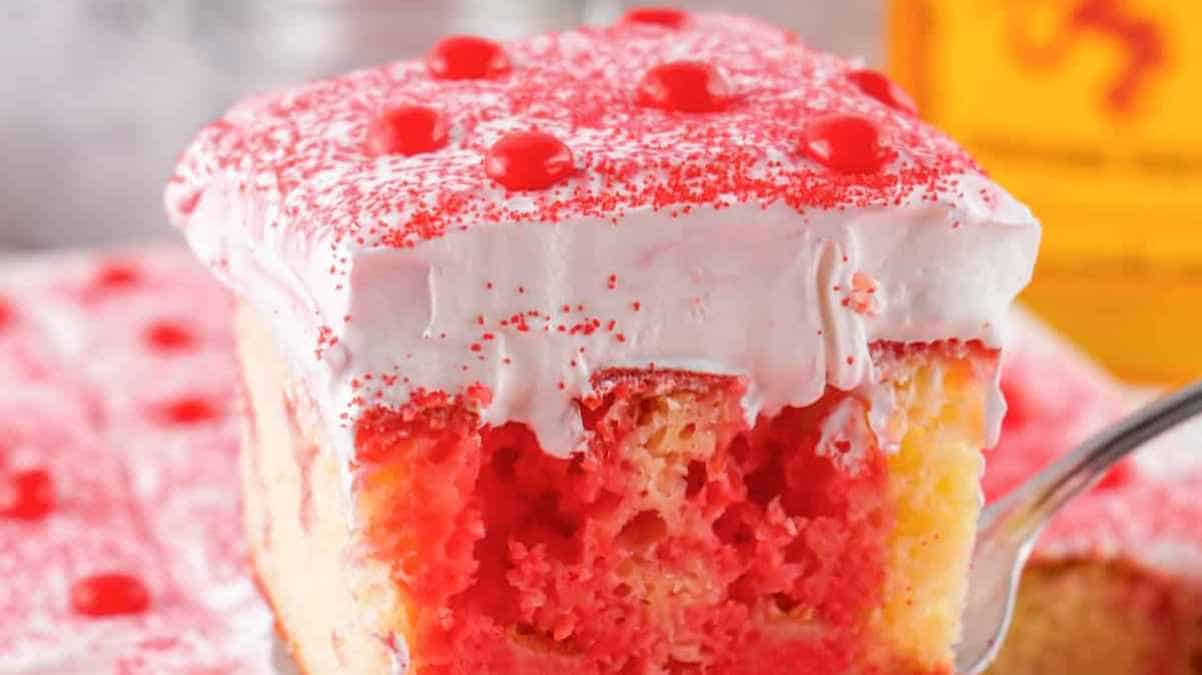 A slice of red and yellow layered cake with white frosting and red sprinkles.